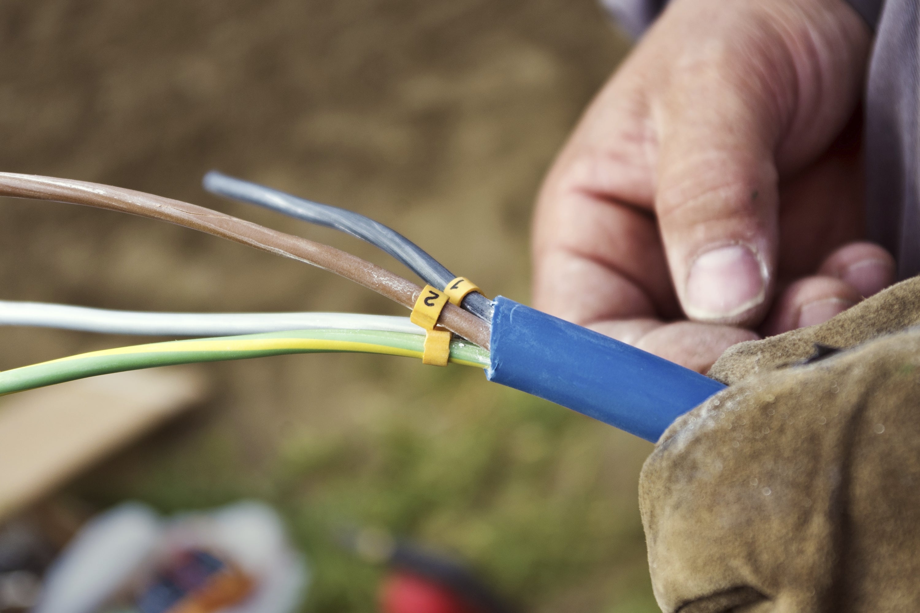 A close-up of a man’s hand holding a cable with exposed wiring. 