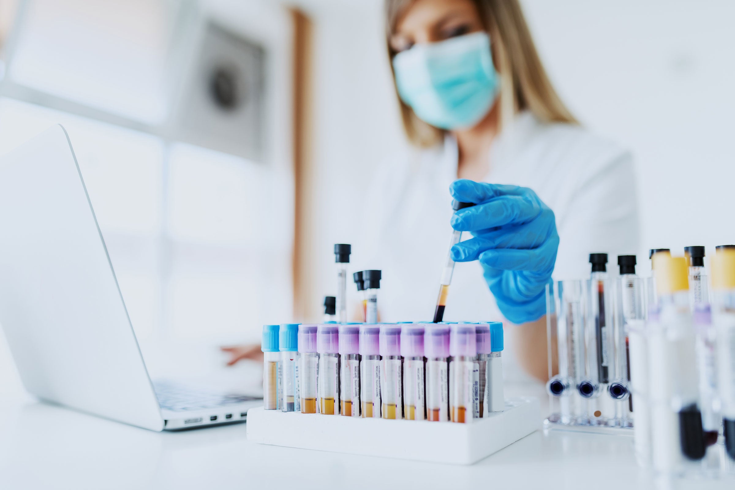 Laboratory technician working on laptop and handling test tubes