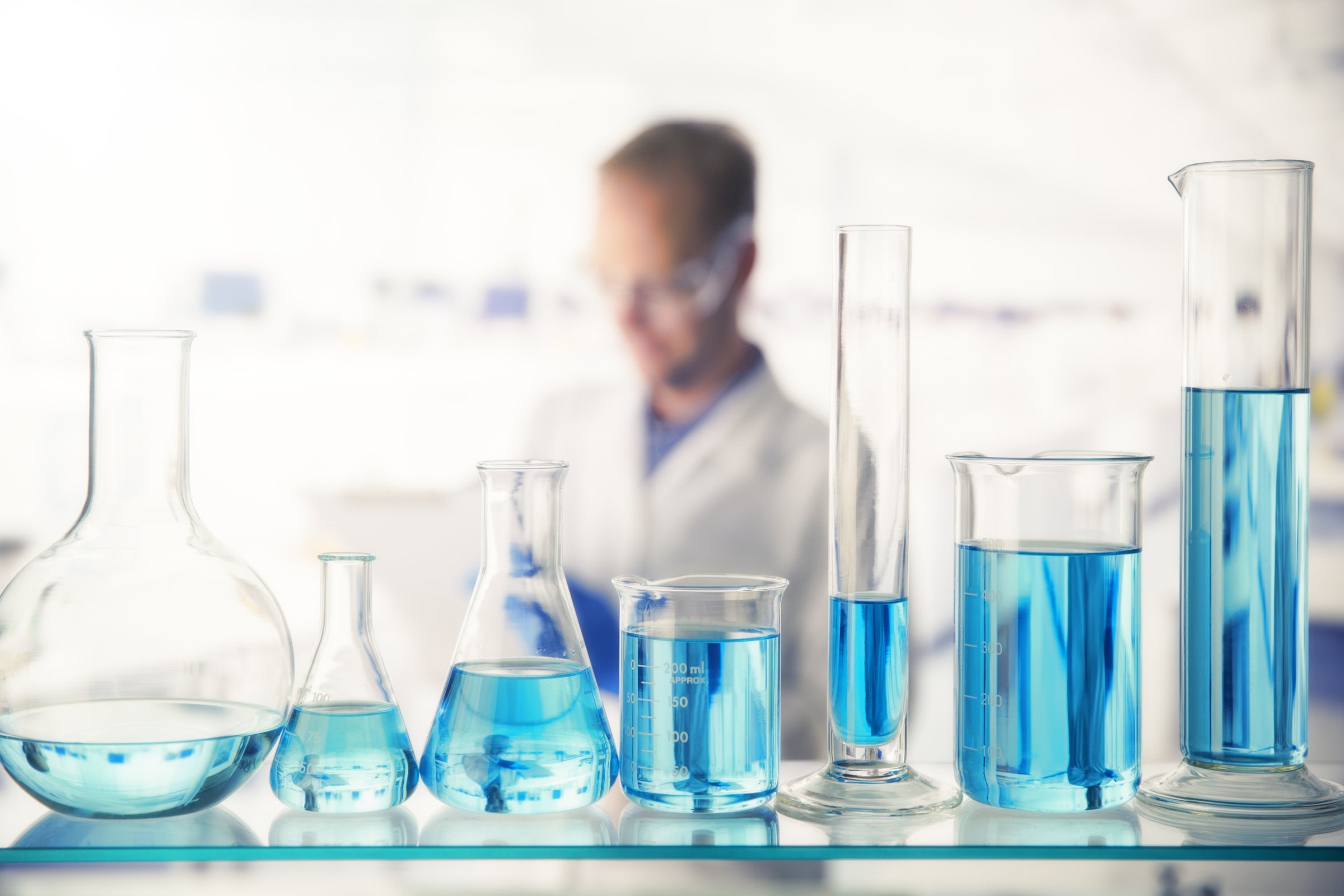 Close up of various solutions in beakers on shelf in lab.