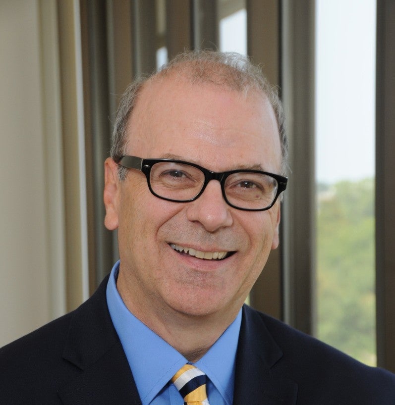 Headshot of Ken Boyce wearing glasses in dark suite with blue shirt. 