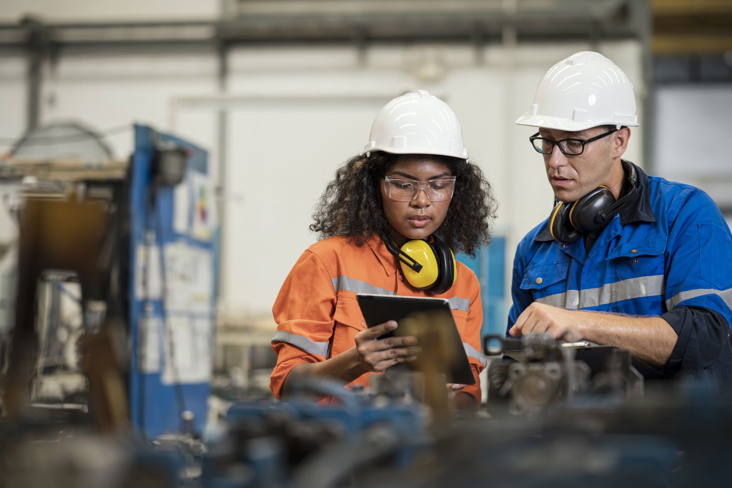 Two manufacturing process engineers in a factory looking at a tablet together.  