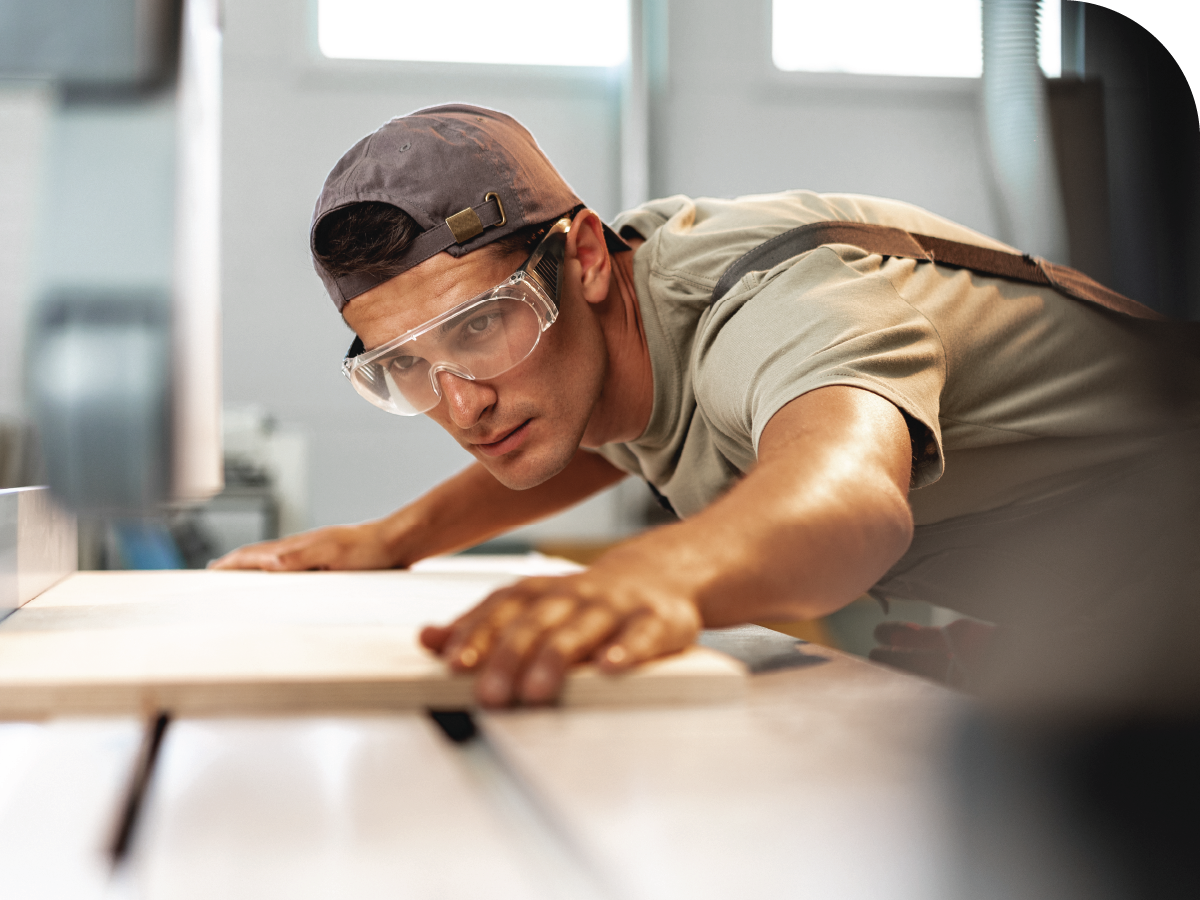 man with safety glasses lining a sheet of wood up for cutting on a table saw