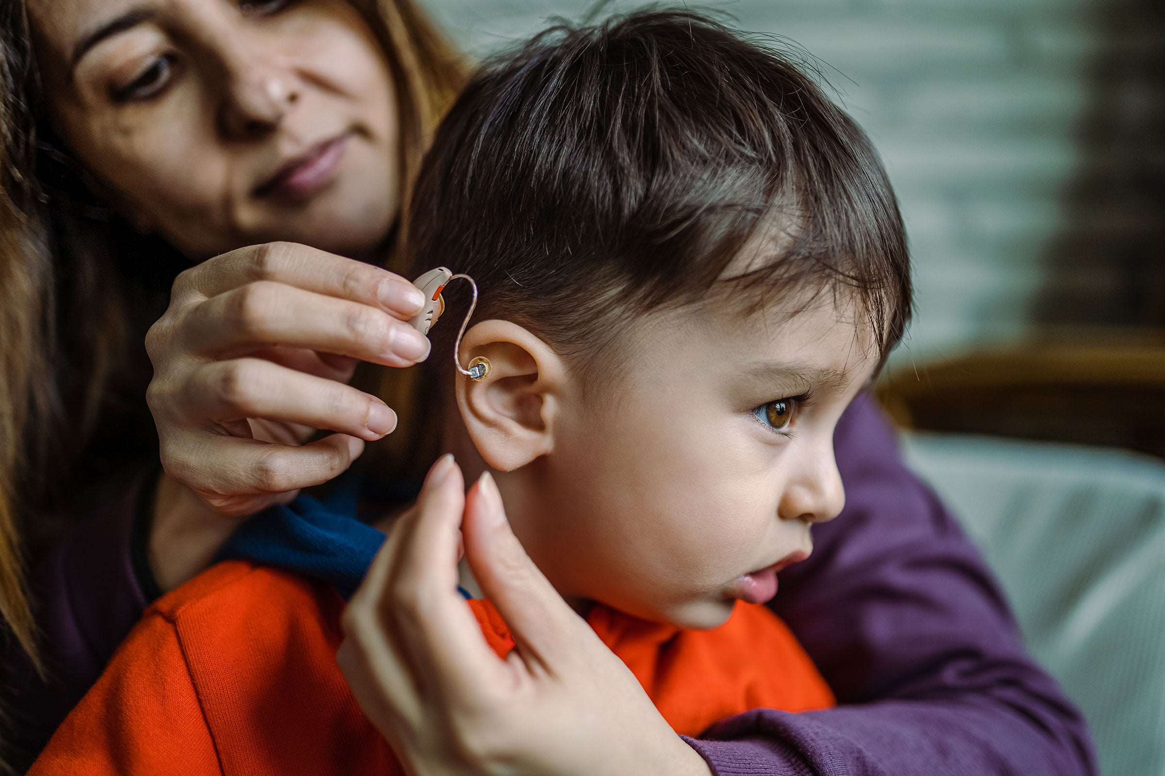 A parent placing a hearing aid onto their child's ear