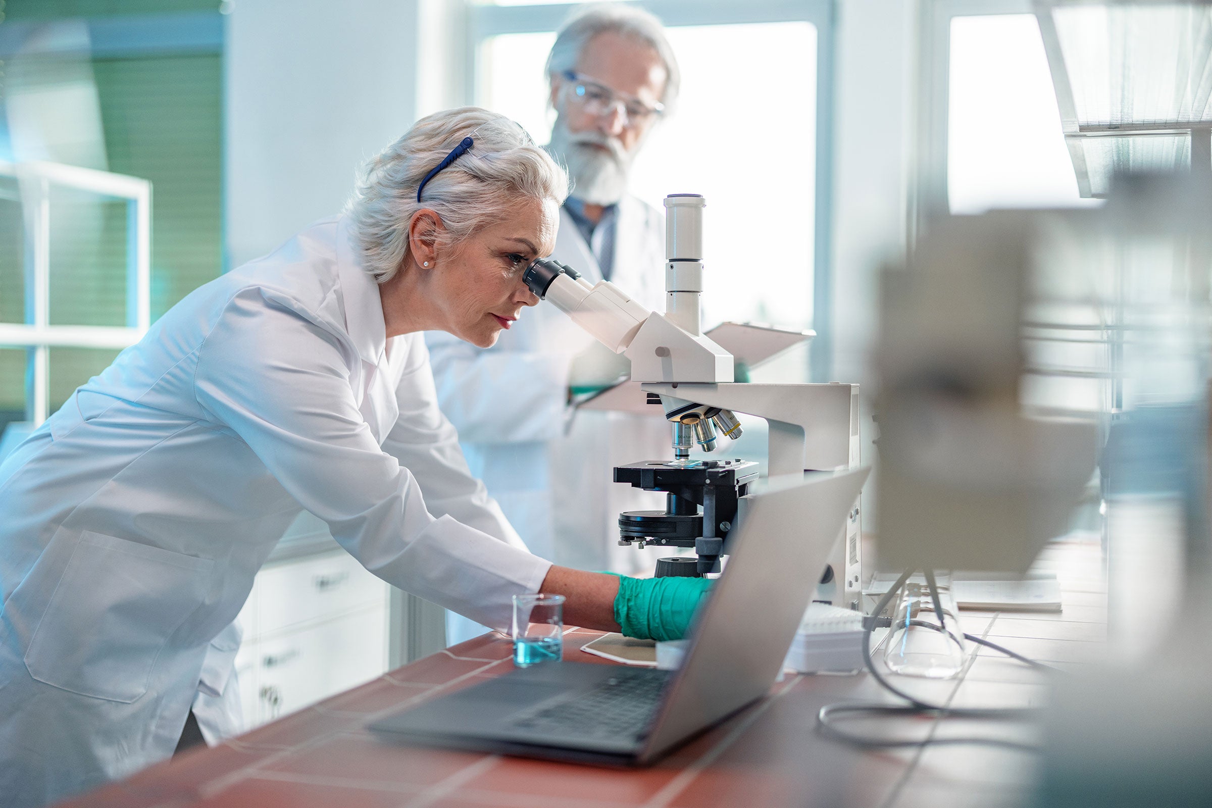 Biochemist using a microscope to review a sample while a colleague watches