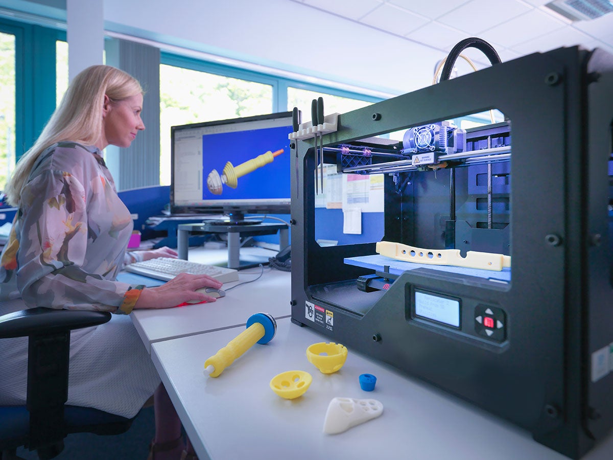 A medical product designer using a 3D printing machine with a CAD design on screen