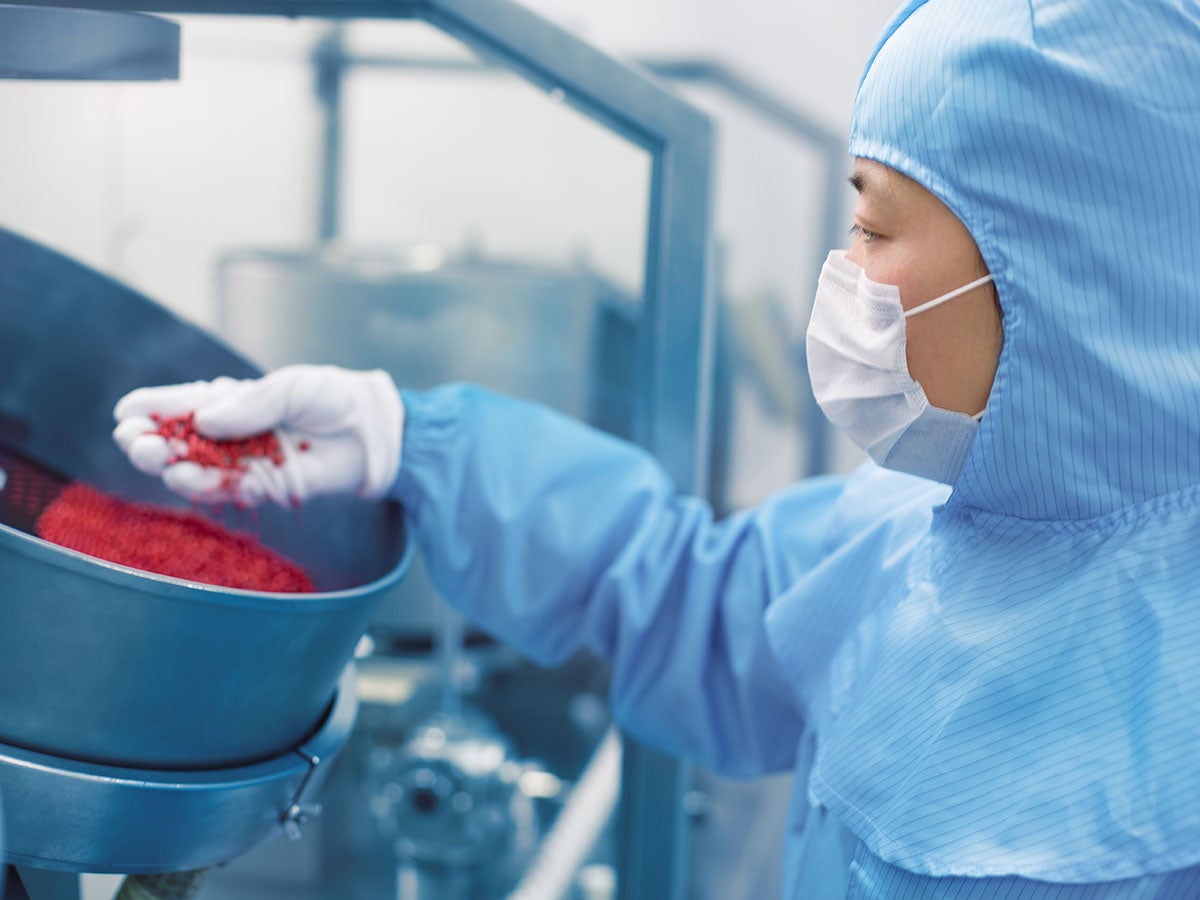 Person in a lab inspecting red plastic pellets