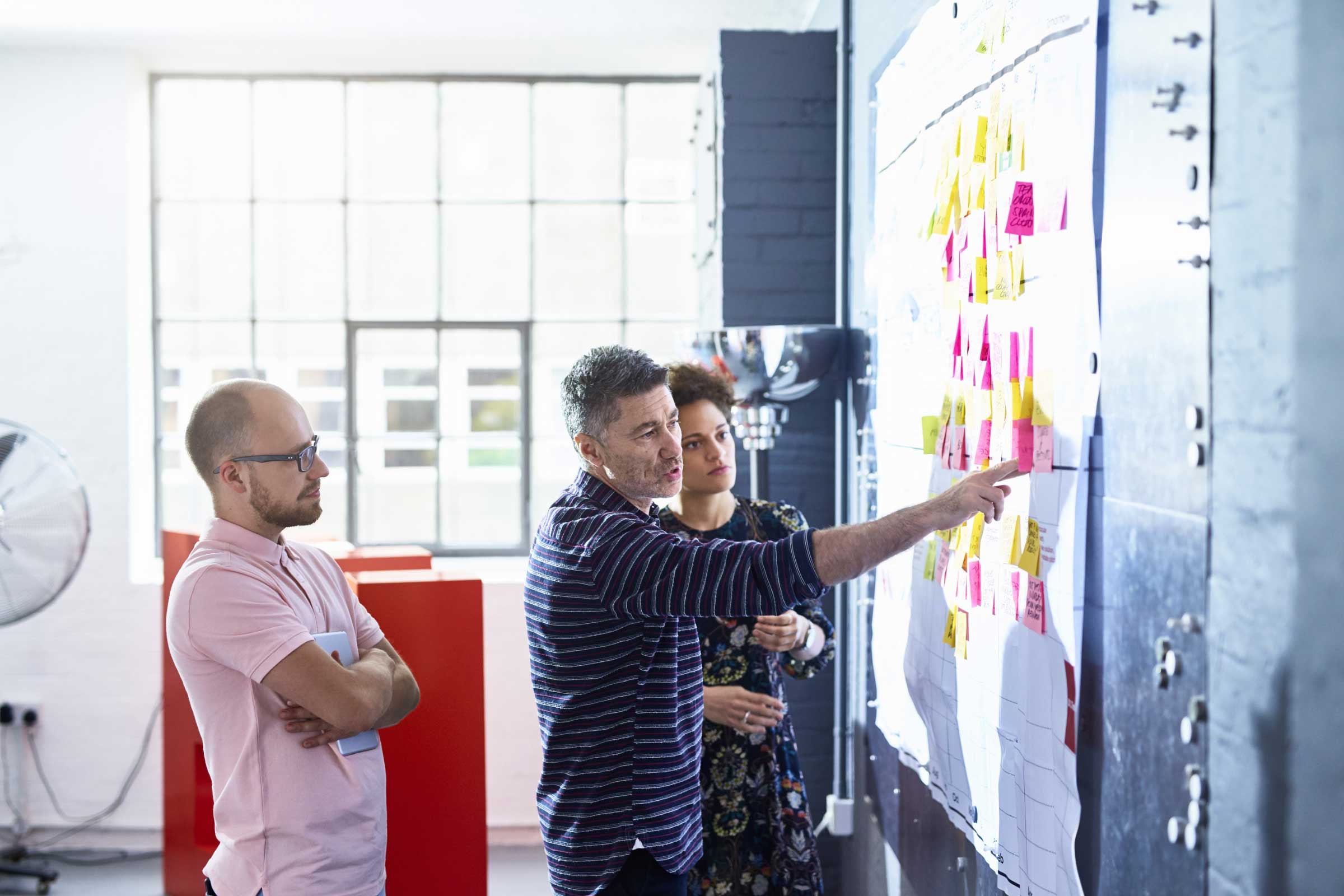 Three coworkers collaborating together in front of a whiteboard covered in post-it notes