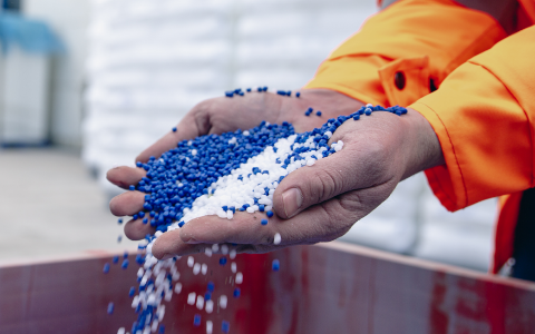 person in warehouse picking up handfuls of blue and white chemical pellets