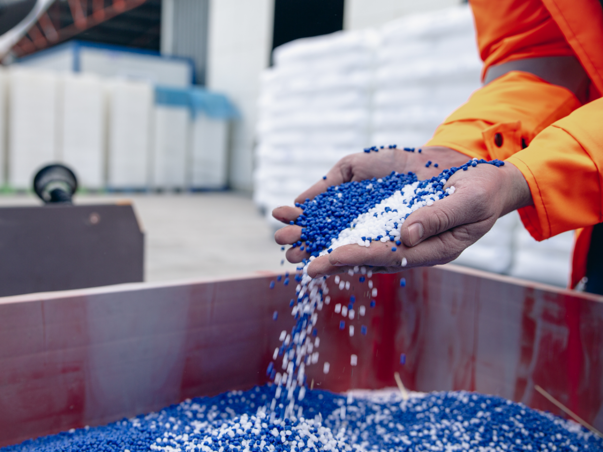 person in warehouse picking up handfuls of blue and white chemical pellets