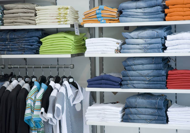 Retail store shelves filled with neatly folded clothes arranged by color. 