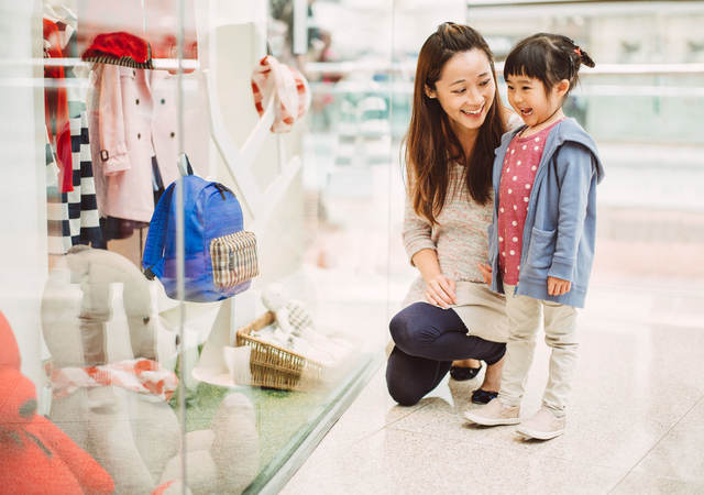 A mother and her daughter look at a clothing store window display in China.