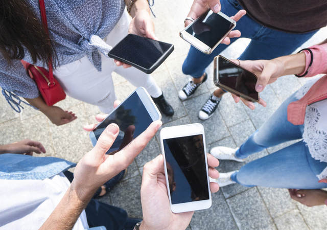 A group of young adults scrolling through their cell phones. 