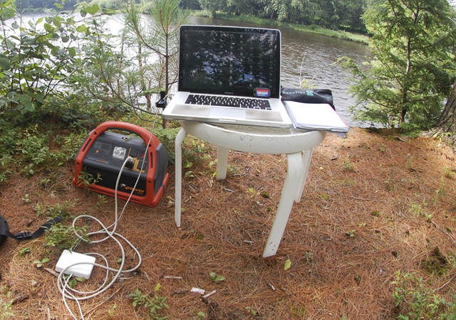 Portable power pack connected to laptop in a nature scene.