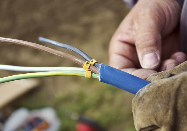 A close-up of a man’s hand holding a cable with exposed wiring. 