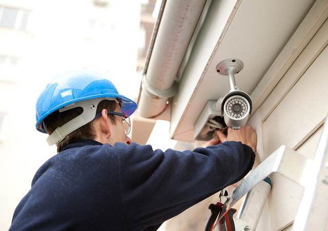 Man in hard hat on a ladder installing an outdoor security camera