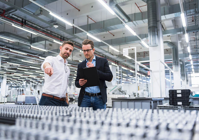 Two men consulting over pallets of plastic products