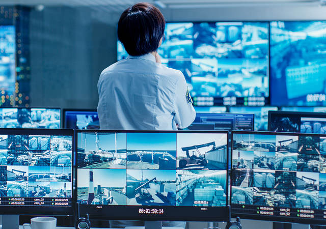 Person standing in a control room looking at security video feeds