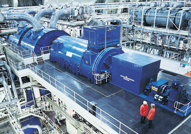 Two workers near an industrial generator in a warehouse setting