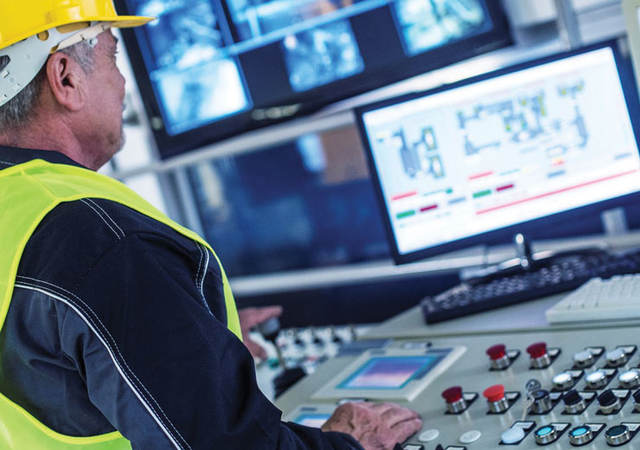 factory worker at a control panel pressing and looking at a monitor