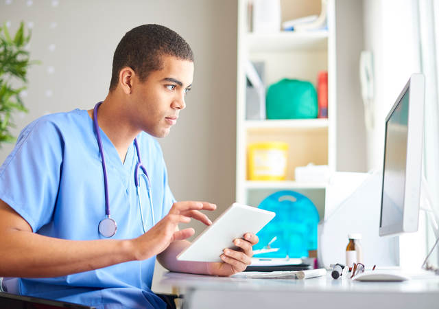 A medical professional reading a chart on a tablet and desktop monitor