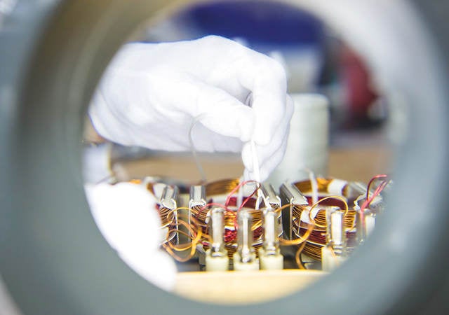 A close-up image of a gloved hand connecting wires in a laboratory setting. 