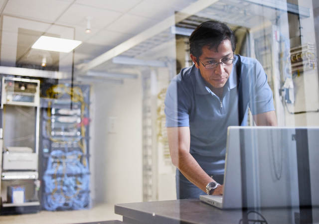 Man using a laptop with an IT server in the background