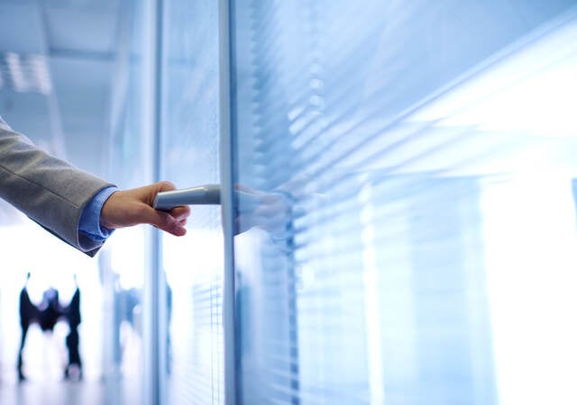 photo of a hand opening an office door, with people in background.