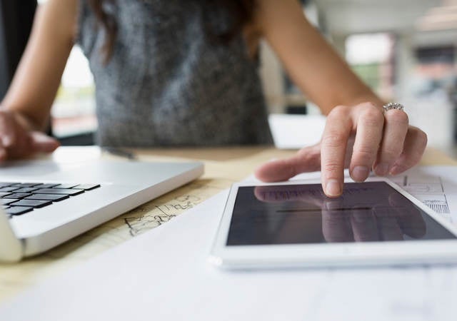 Close up of female architect at laptop using digital tablet in office