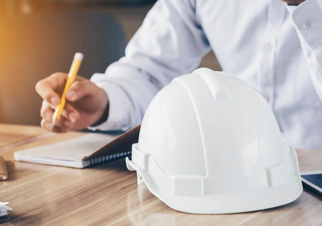 Photo of a person making notes, hard hat in foreground