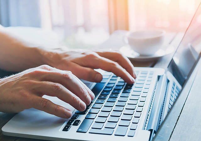 Photo of a man typing on a laptop keyboard