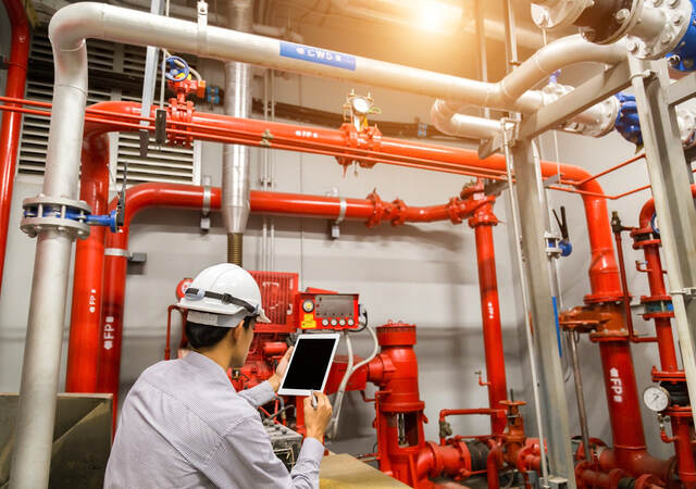 Engineer with tablet checks red generator pump for water sprinkler piping and fire alarm control system.