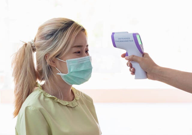 Lady wearing a mask getting temp scanned