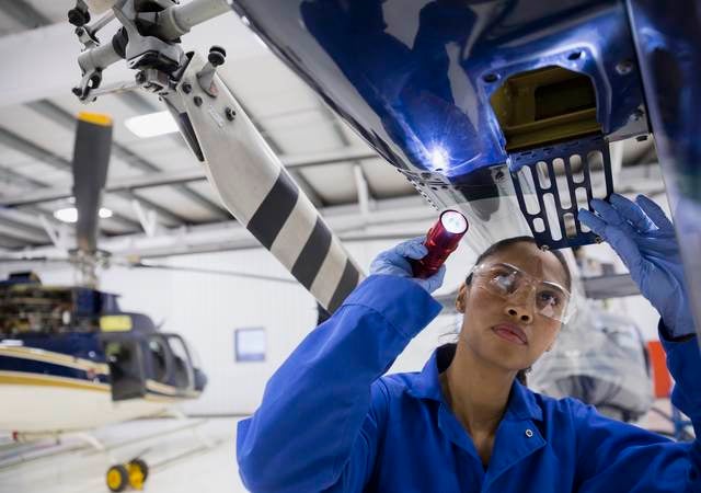 Female helicopter mechanic examining part with flashlight