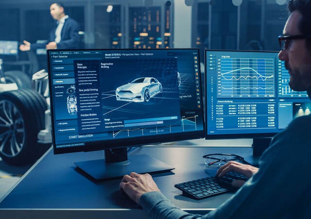 Automotive engineer looking at a computer displaying a 3D electric car chassis prototype with wheels.