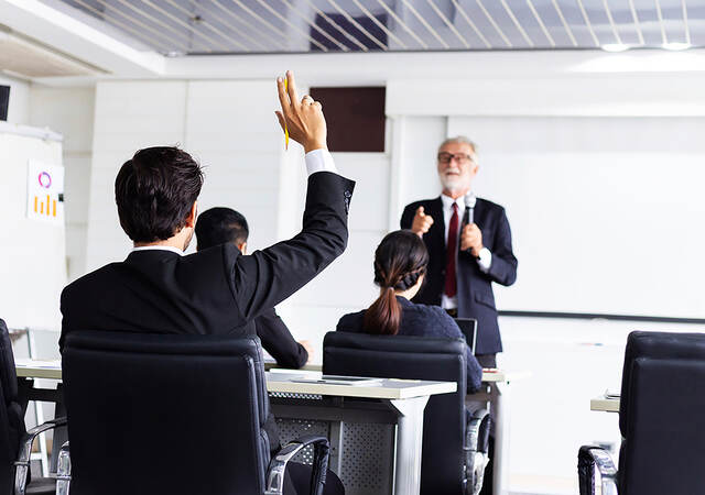 Business man raising hand in a classroom setting