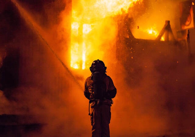 A firefighter sprays water on the outside of a burning building