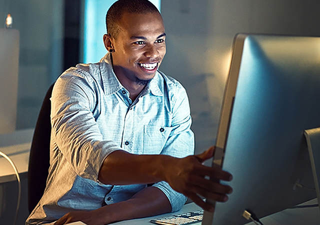 Smiling man sitting at a desk in front of a computer monitor