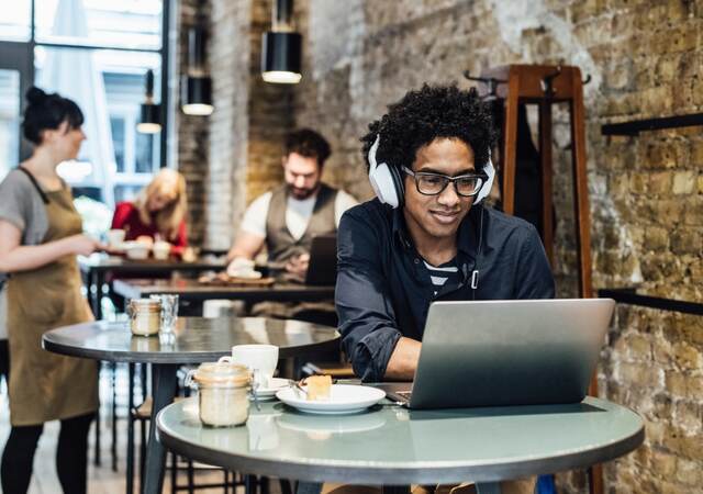 Man working on a computer wearing headphones in a cafe