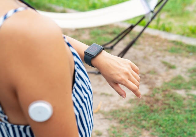 Young woman with wearable patch on arm checking a smartwatch to see her blood sugar level.