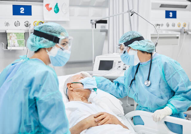 Medical professionals wearing personal protection equipment (PPE) attending to a hospital patient