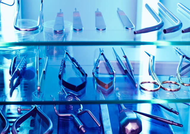 Medical tools sit on a shelf under the blue glow of ultraviolet light, used as a germicidal disinfectant.