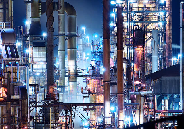 A brightly lit commercial oil refinery is shown at night.