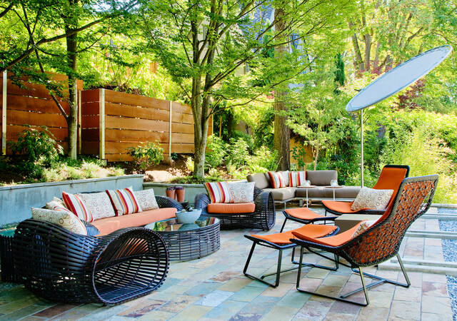 Outdoor furniture including sofa, chairs, table and umbrella in a sunny patio setting