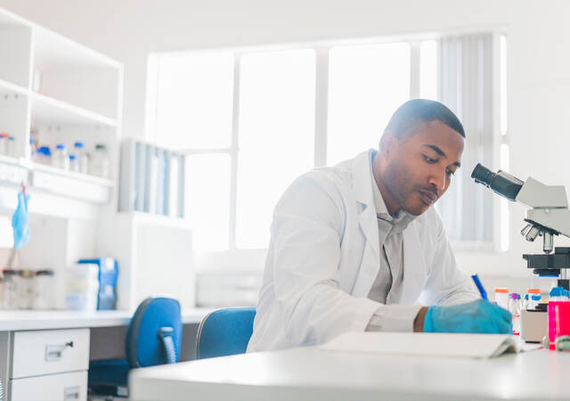 Chemist making reports by microscope at laboratory