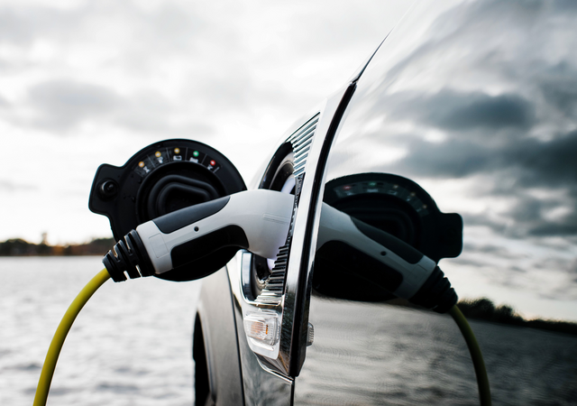 Black electric car overlooking coastal waterway while charging on a cloudy day