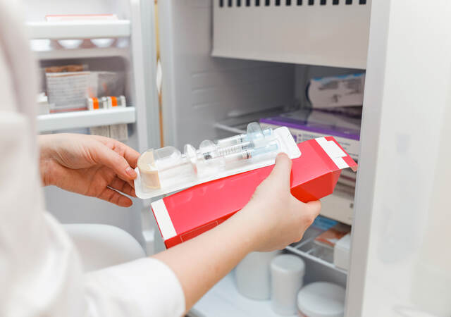 The doctor takes out medicine from the refrigerator with a disposable syringe