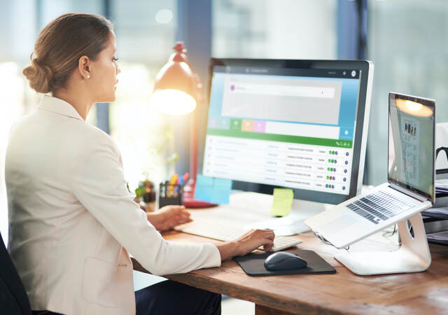 Woman sitting at desk in front of a computer monitor and laptop computer