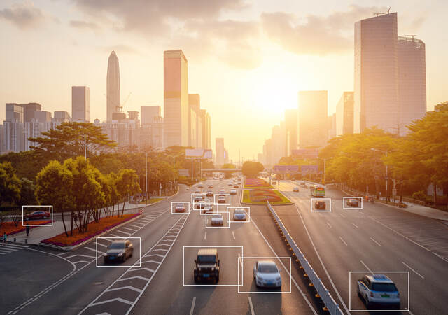 Cars highlighted by artificial intelligence driving down highway with high-rise buildings in the distance