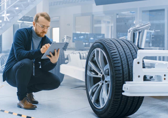 Engineer in an automotive laboratory works on a tablet and evaluates a car prototype