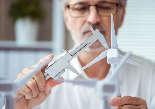 Person measuring a scale model of a wind turbine with calipers